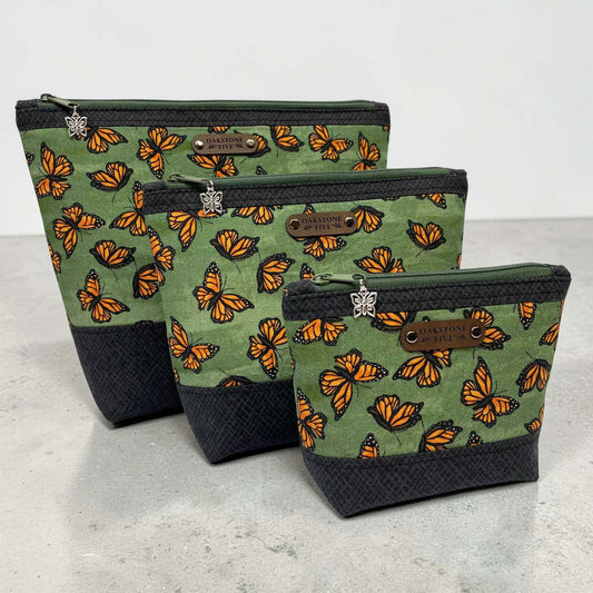 Set of three green pouches with monarch butterfly pattern on a gray surface