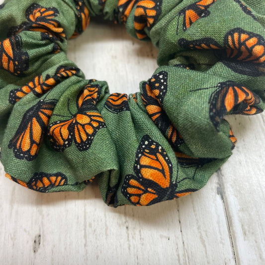 A close-up of a green hair scrunchie with orange and black monarch butterfly pattern on a wooden table