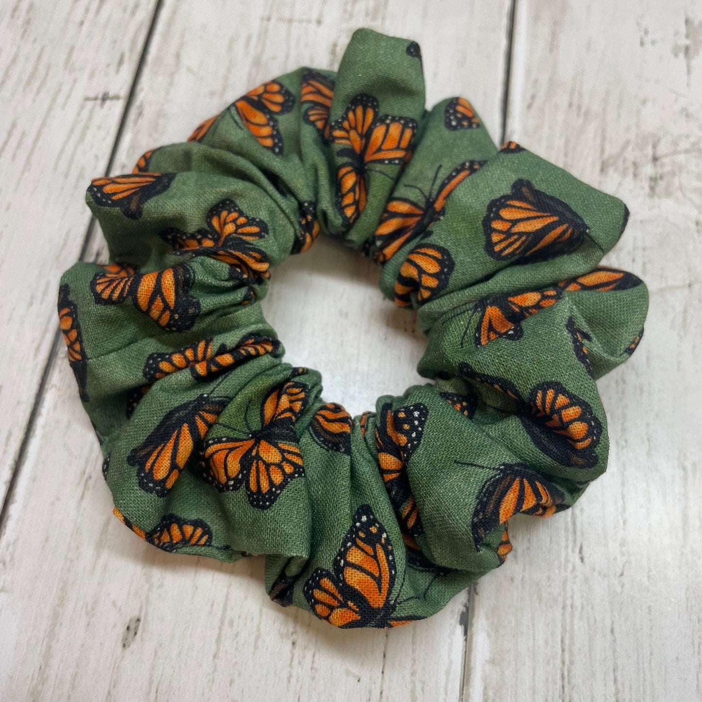 Green hair scrunchie with orange and black monarch butterfly pattern on a wooden table