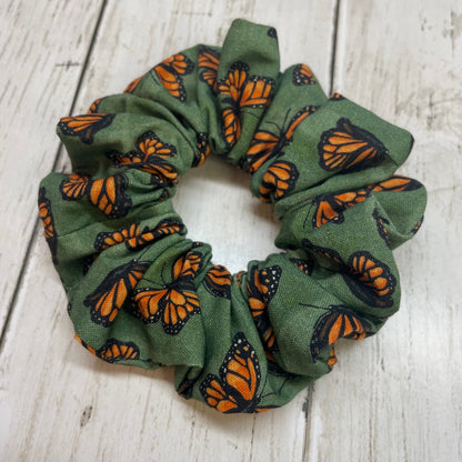 Green hair scrunchie with orange and black monarch butterfly pattern on a wooden table