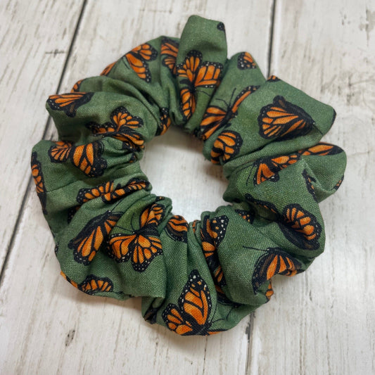 Green hair scrunchie with orange and black monarch butterfly pattern on a wooden table