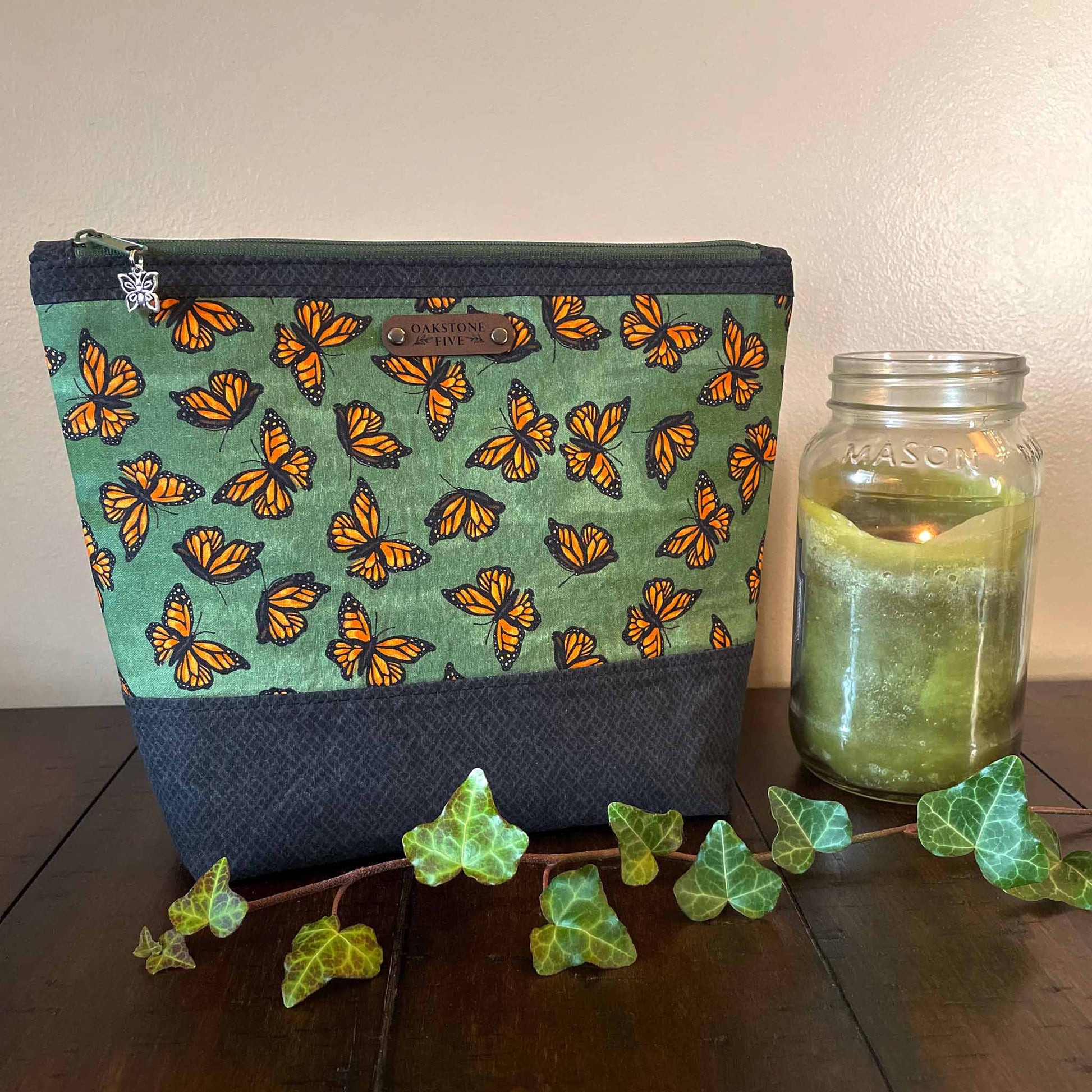 Large-size zipper pouch with monarch butterfly pattern next to a mason jar candle on a wooden surface.