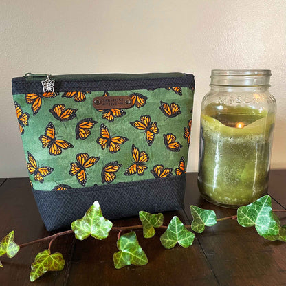 Medium-sized zipper pouch with monarch butterfly pattern next to a mason jar candle on a wooden surface.
