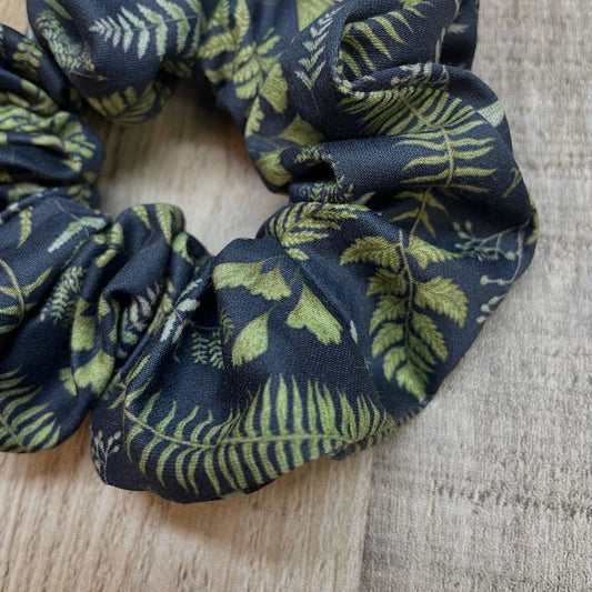 Close-up of a navy blue organic cotton scrunchie with green leaf and fern pattern on a wooden surface