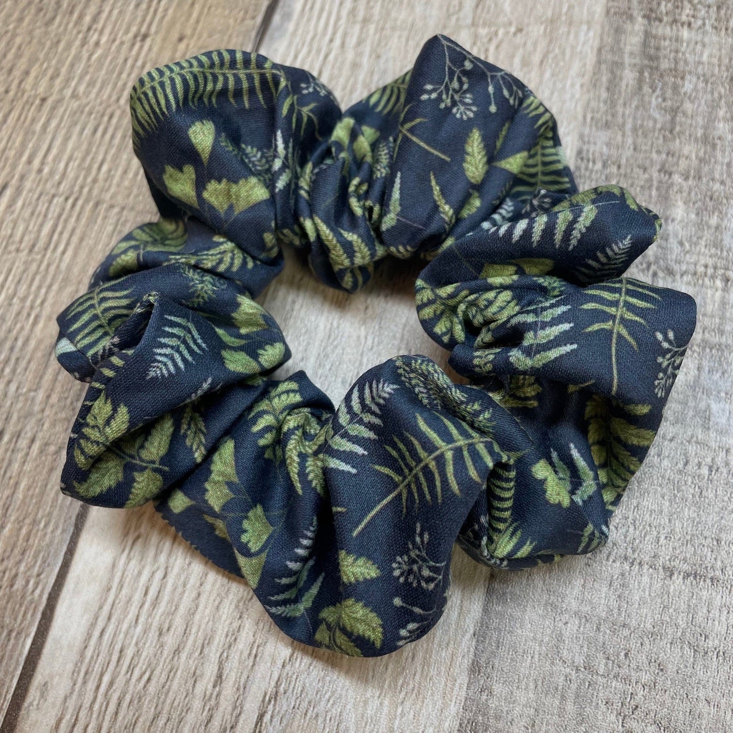 Navy blue organic cotton scrunchie with green leaf and fern pattern on a wooden surface