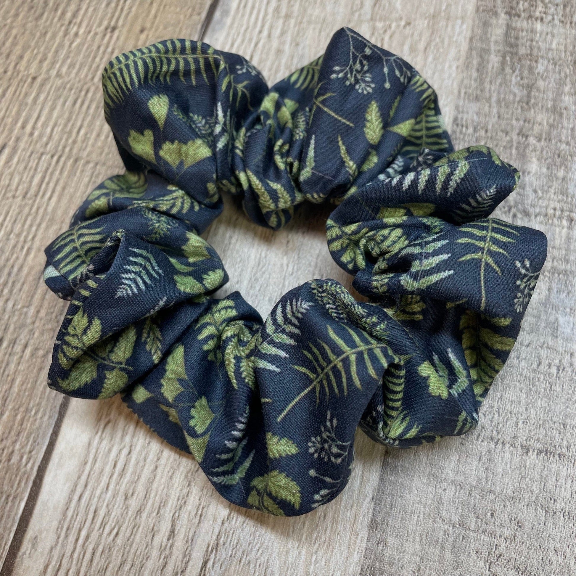 Navy blue organic cotton scrunchie with green leaf and fern pattern on a wooden surface