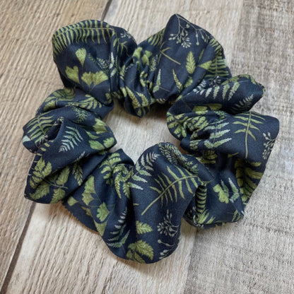 Navy blue organic cotton scrunchie with green leaf and fern pattern on a wooden surface
