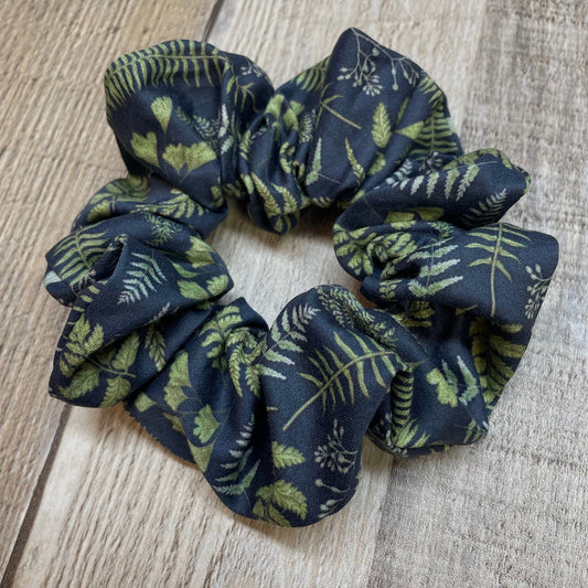 Navy blue organic cotton scrunchie with green leaf and fern pattern on a wooden surface