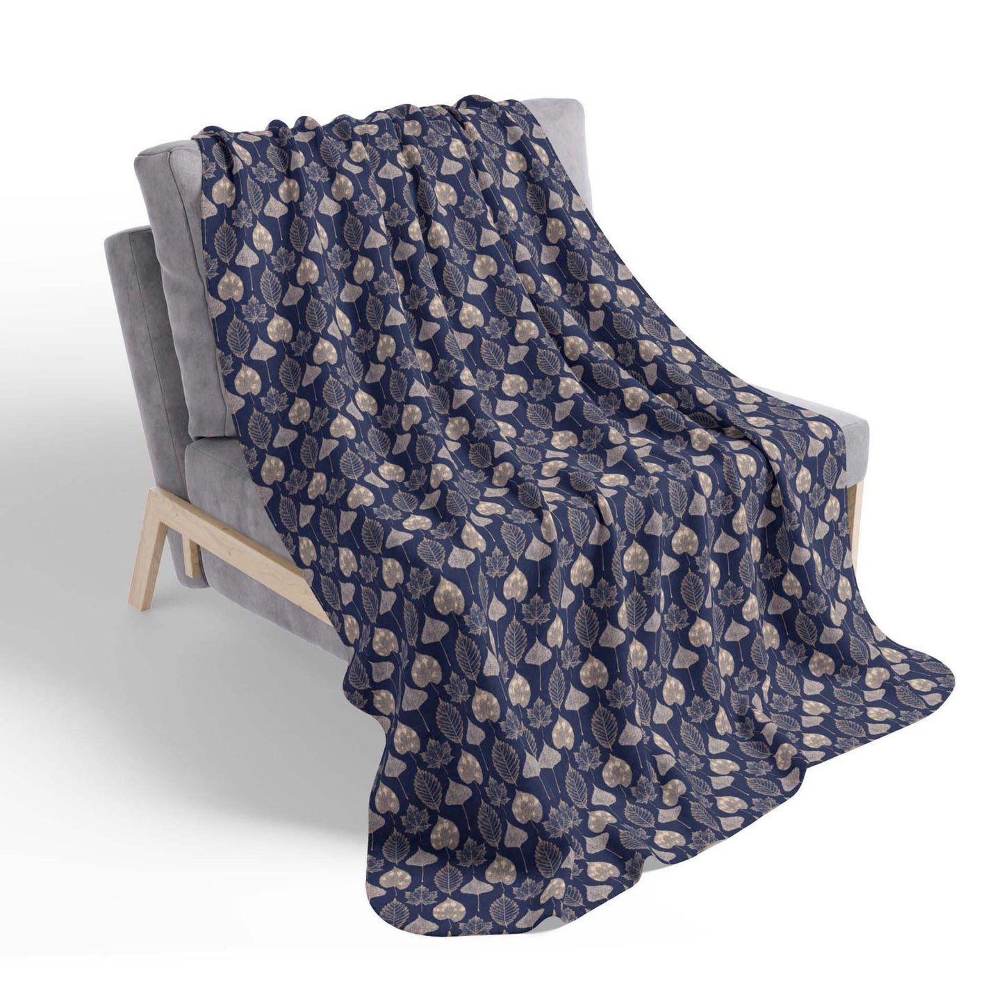 A navy blue, leaf-patterned sherpa throw blanket, draped over a chair on a white background