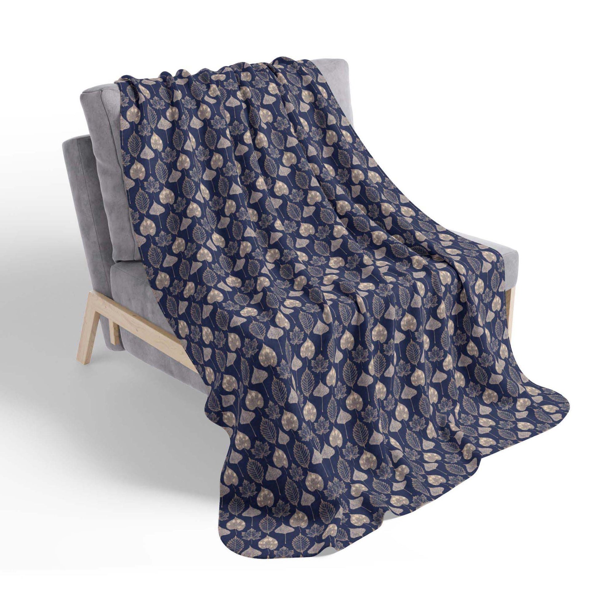 A navy blue, leaf-patterned sherpa throw blanket, draped over a chair on a white background