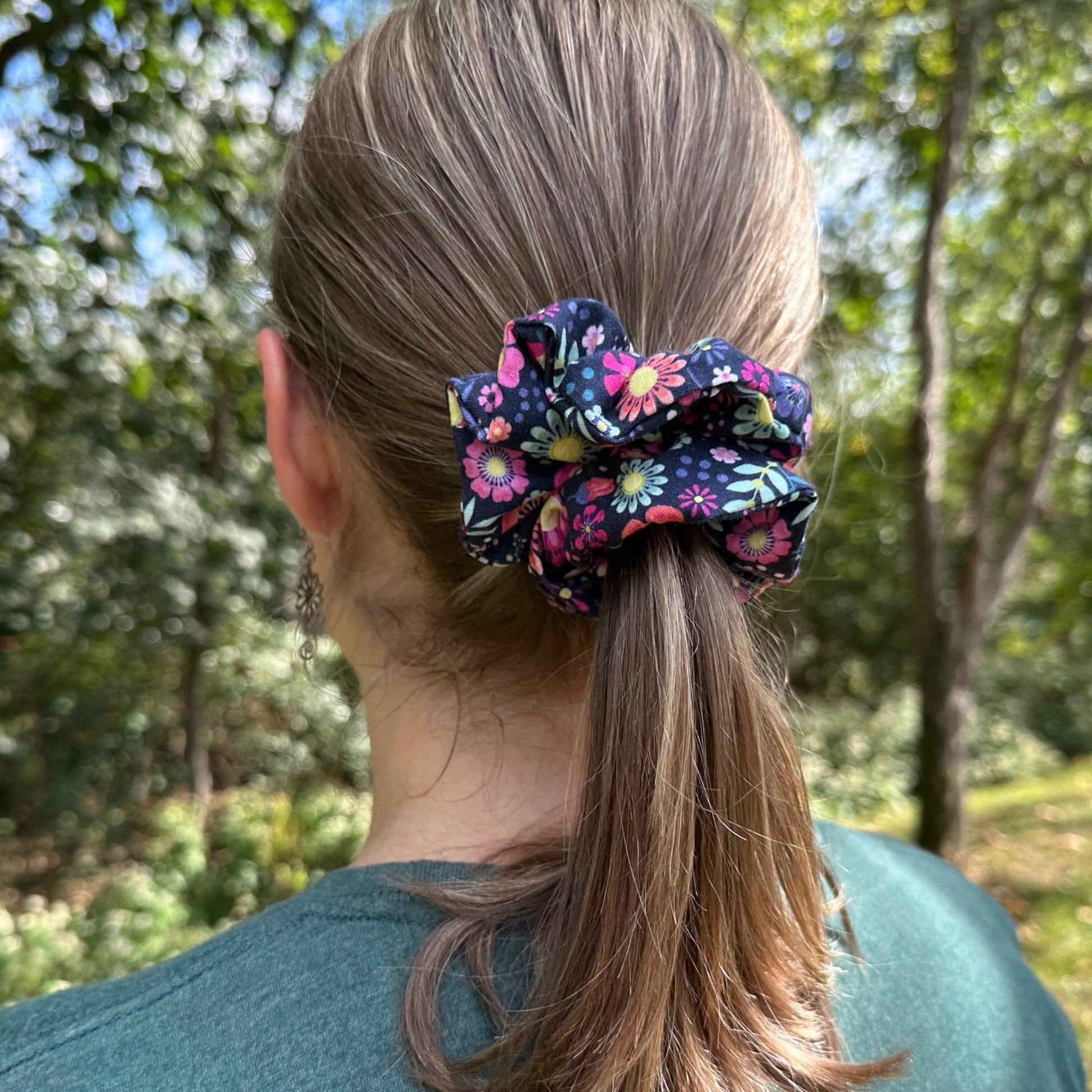 Woman standing outside wearing a cute navy and pink floral hair scrunchie in her ponytail.