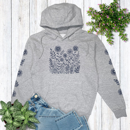 Gray hoodie with floral design on the front and on both sleeves, laying on a wooden surface with plants around