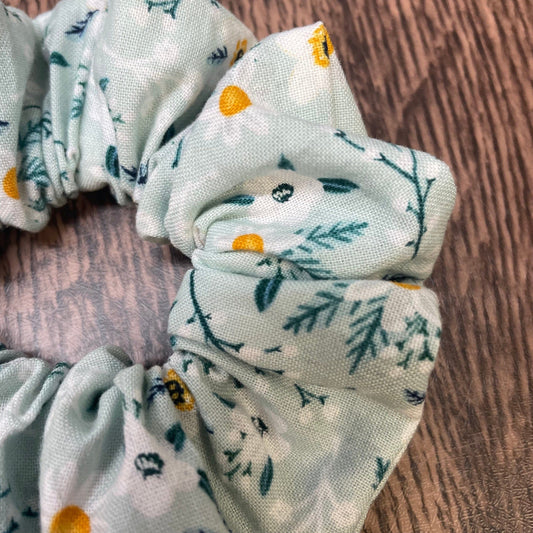 A close-up of a green floral patterned scrunchie on a wooden surface