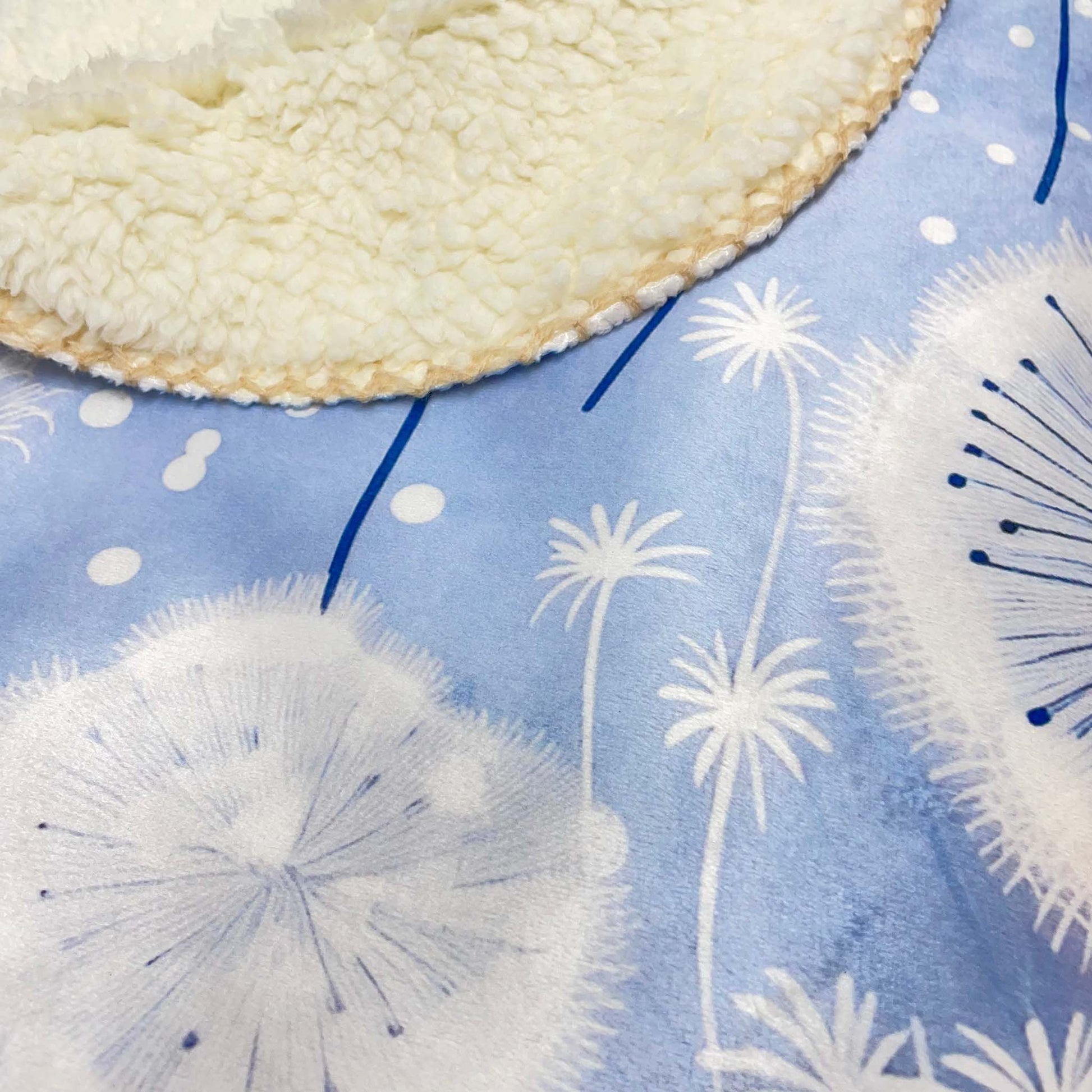 Close-up of a sherpa blanket with a blue background featuring white dandelion pattern.