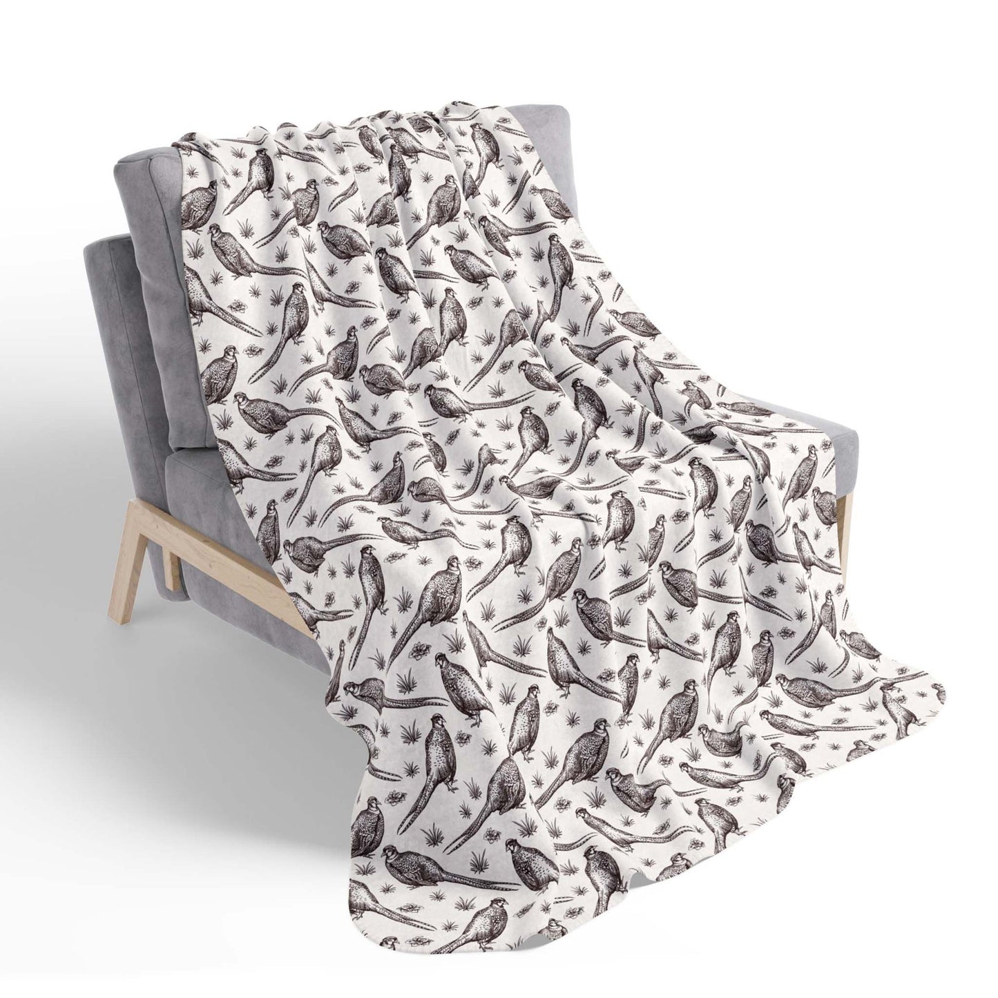 An ivory Sherpa blanket with illustrations of pheasants on the front , laying draped over a chair, on a white background