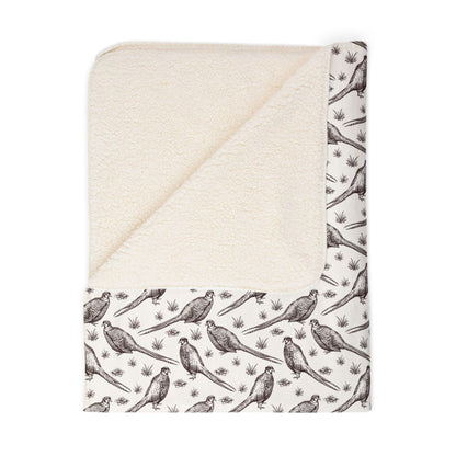 Folded ivory Sherpa blanket with illustrations of pheasants on the front and sherpa fleece on the backside, on a white background