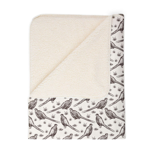 Folded ivory Sherpa blanket with illustrations of pheasants on the front and sherpa fleece on the backside, on a white background