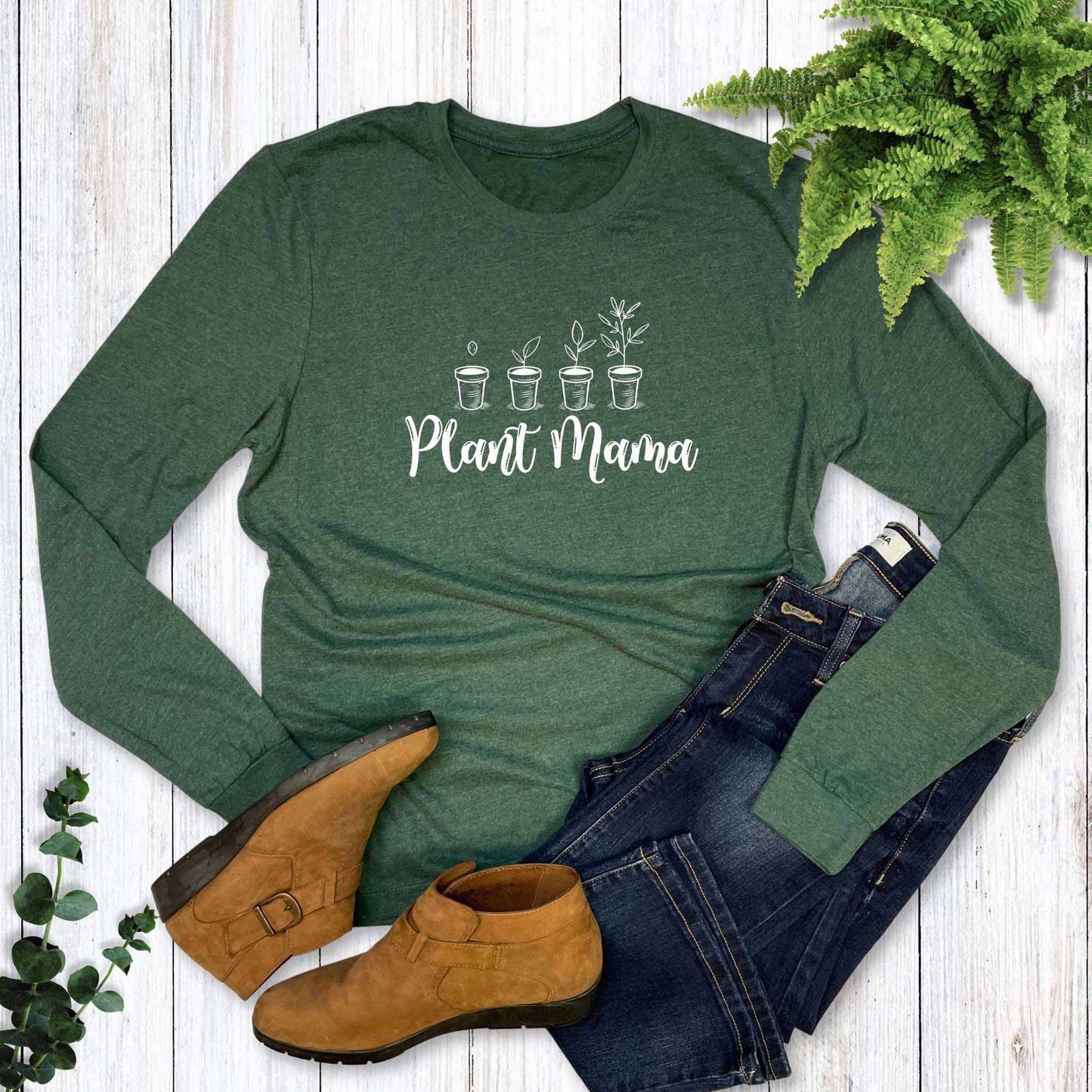 Green long-sleeve shirt with 'Plant Mama' text, paired with brown boots and blue jeans on a wooden surface.