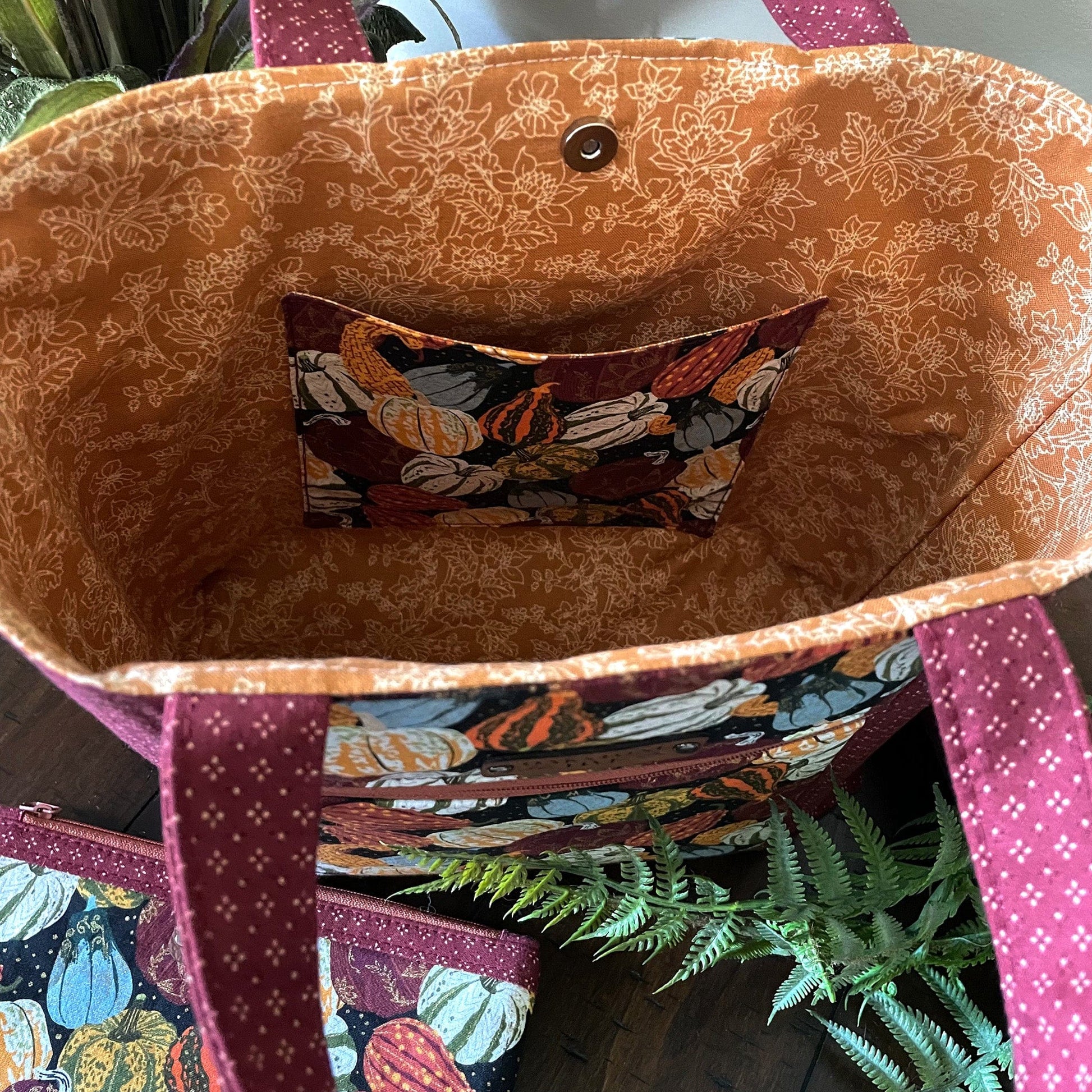Close-up of the inside of a beautiful, handmade seasonal tote bag with pumpkin and gourd fall pattern and matching zipper pouch, siting on a table with a fern.