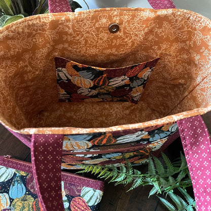 Close-up of the inside of a beautiful, handmade seasonal tote bag with pumpkin and gourd fall pattern and matching zipper pouch, siting on a table with a fern.