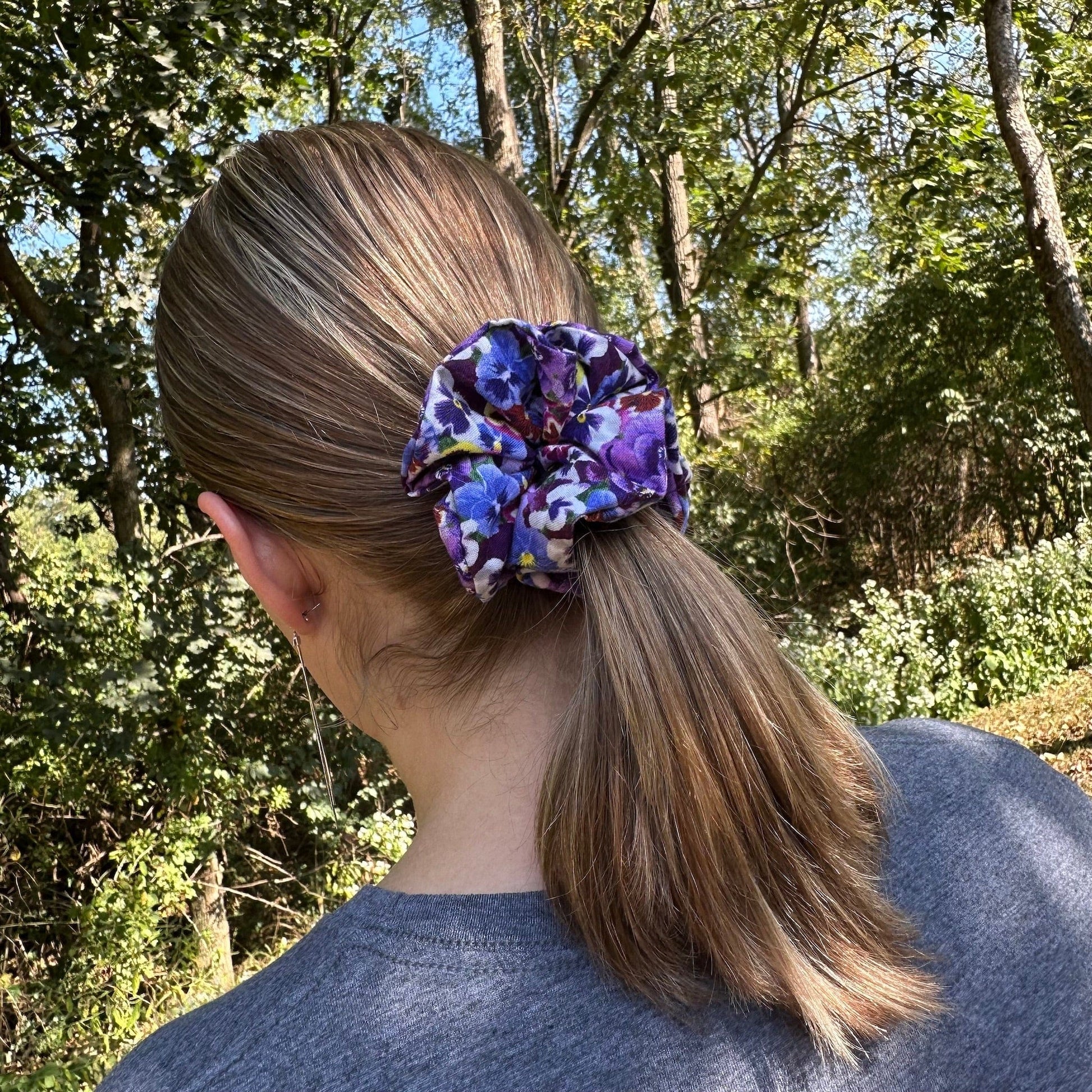 Girl standing outside wearing a pretty purple, floral scrunchies that has a vibrant pansies pattern