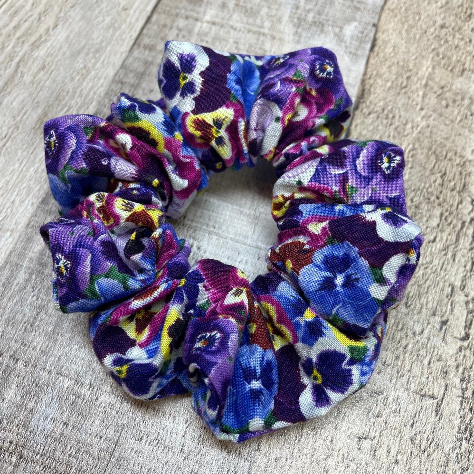 Floral, purple pansies patterned scrunchie on a wood surface