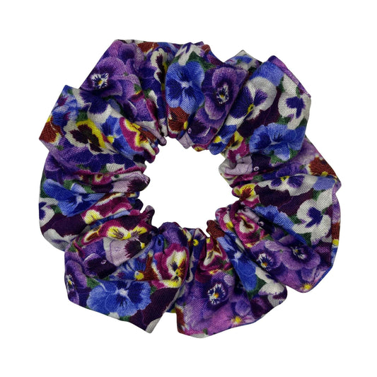 A handmade, purple pansies cotton hair scrunchie on a white background.