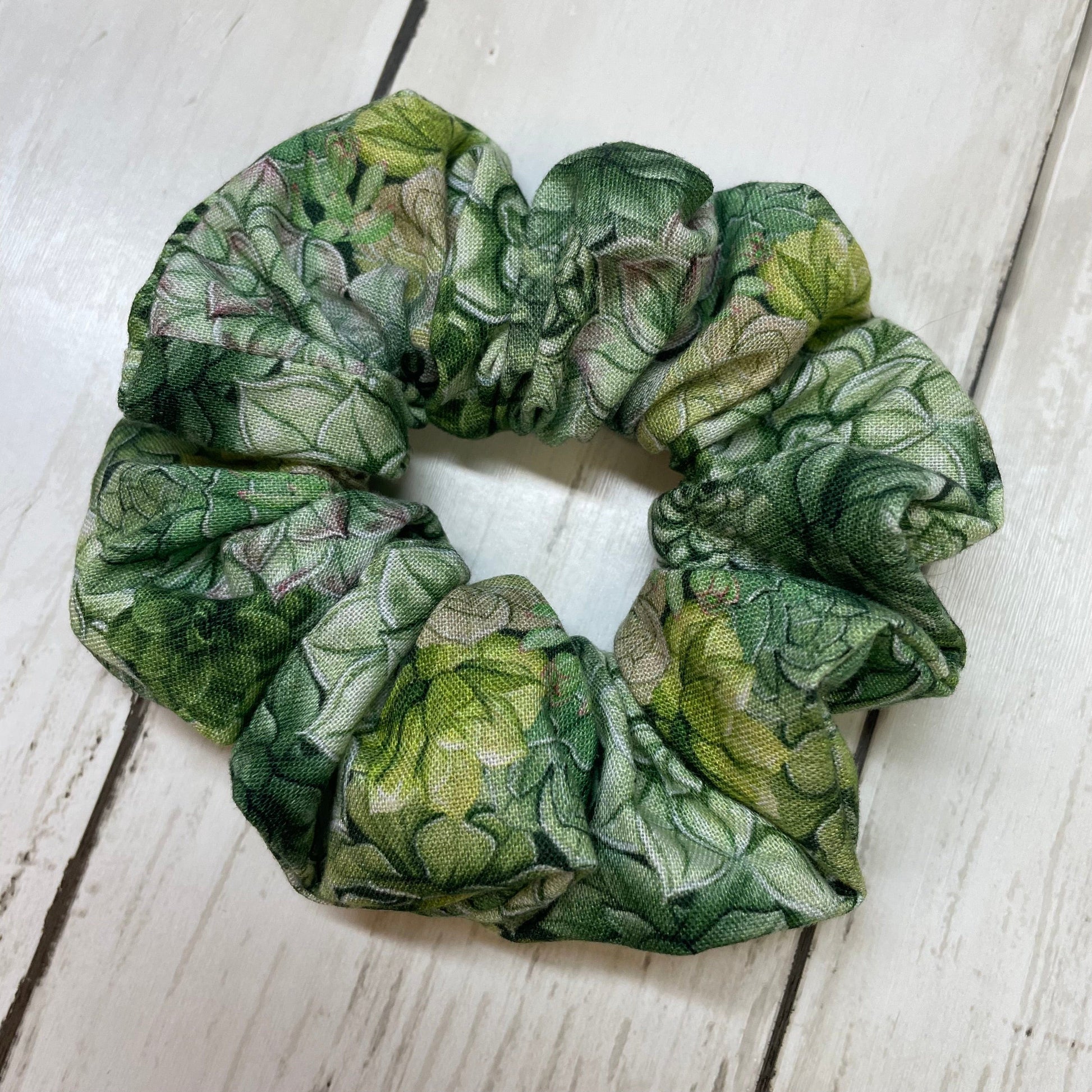 A green, handmade scrunchie with a plant succulent pattern laying on a wooden surface
