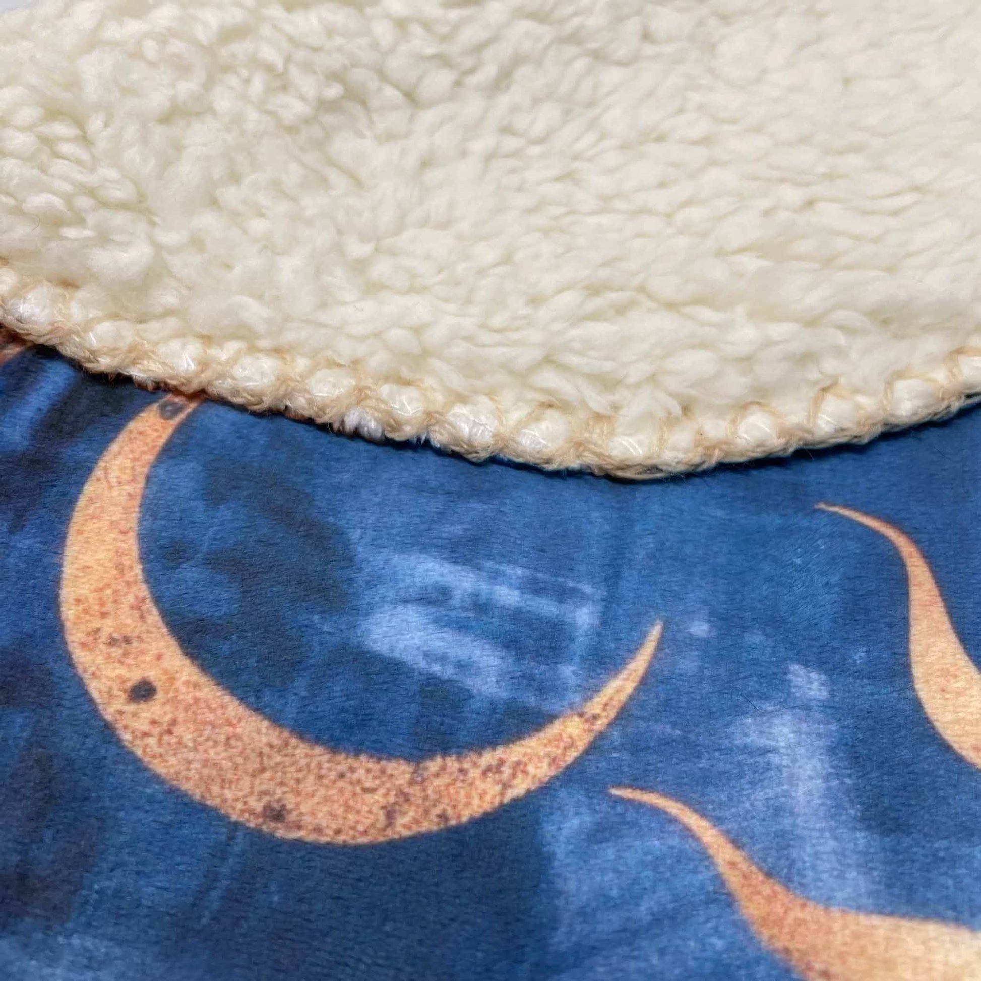 Close-up of a sherpa blanket with a blue background featuring gold crescent sun and moon designs.