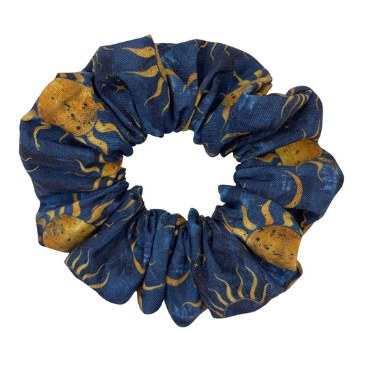 A blue, handmade scrunchie with a sun, moon, and stars pattern.