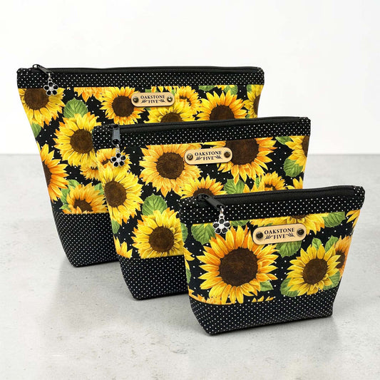Three sunflower-patterned zipper bags with black polka dot accents on a light gray background
