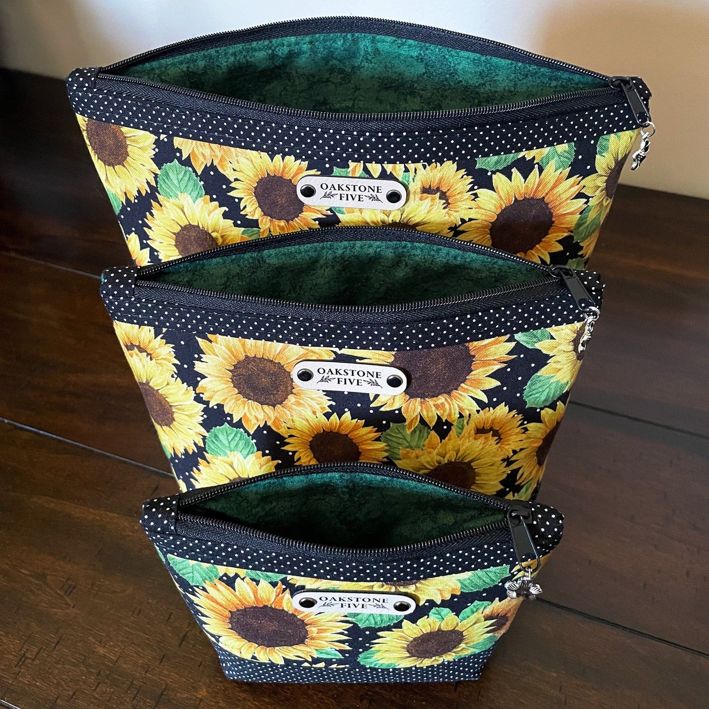 Three sunflower zipper pouches, unzippered showing the liner fabric, on a wooden surface
