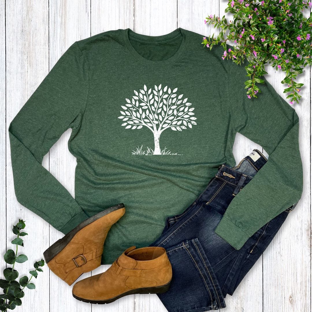 Green long-sleeve shirt with a white tree design, paired with brown boots and blue jeans on a wooden surface.