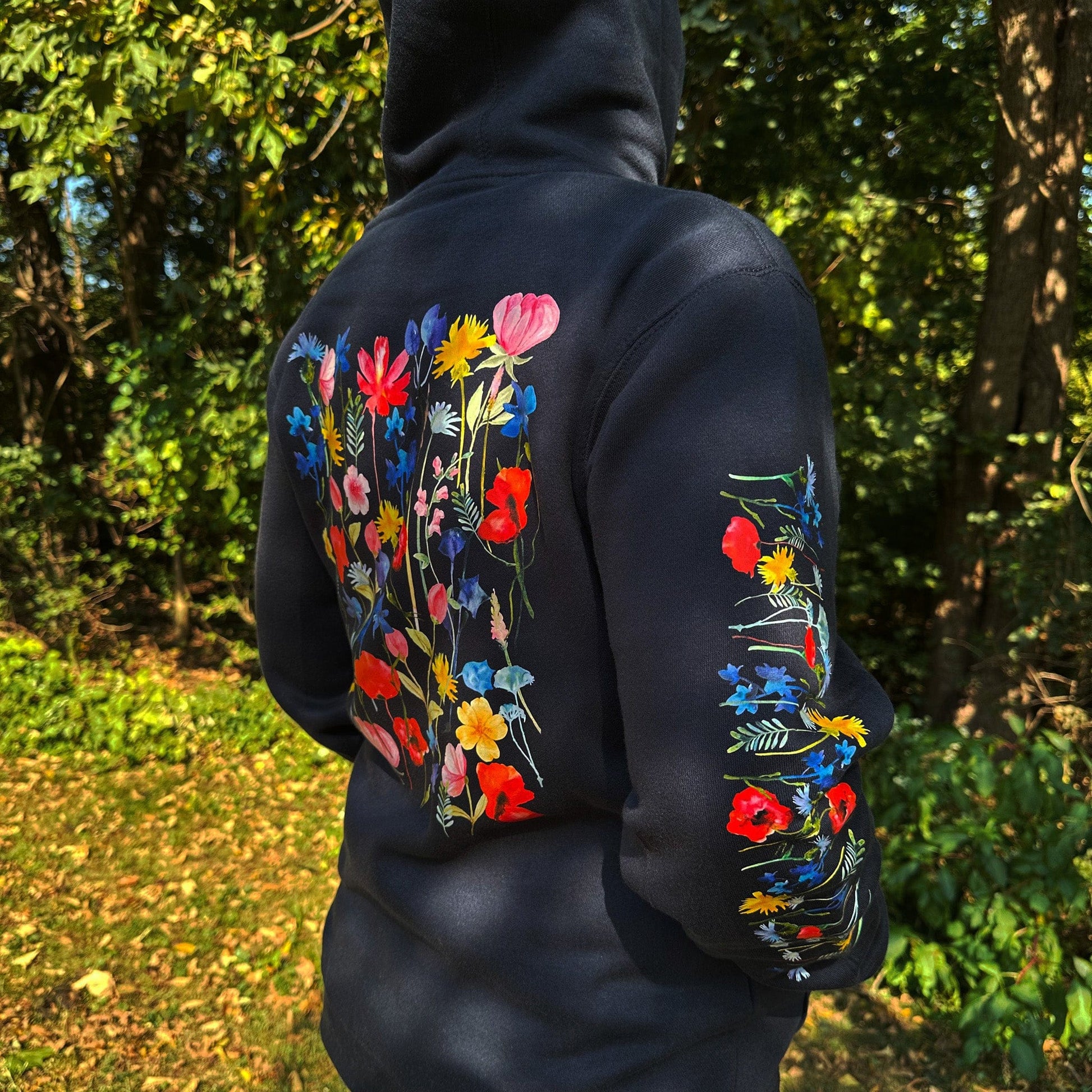 Woman wearing a navy hoodie with floral designs on the sleeves and back, standing outdoors.