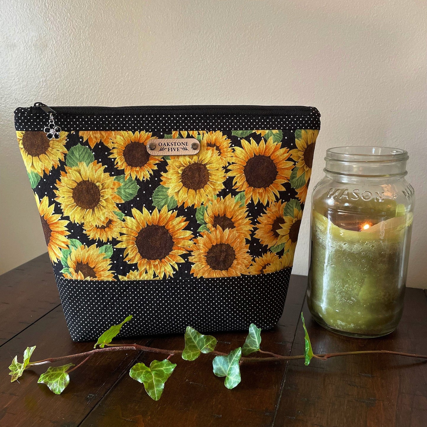 A large sunflower zipper pouch on a wooden surface with a candle and ivy