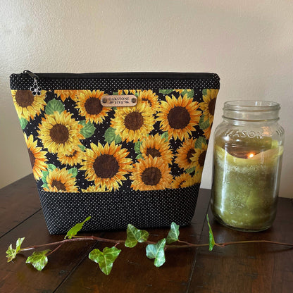 A large sunflower zipper pouch on a wooden surface with a candle and ivy