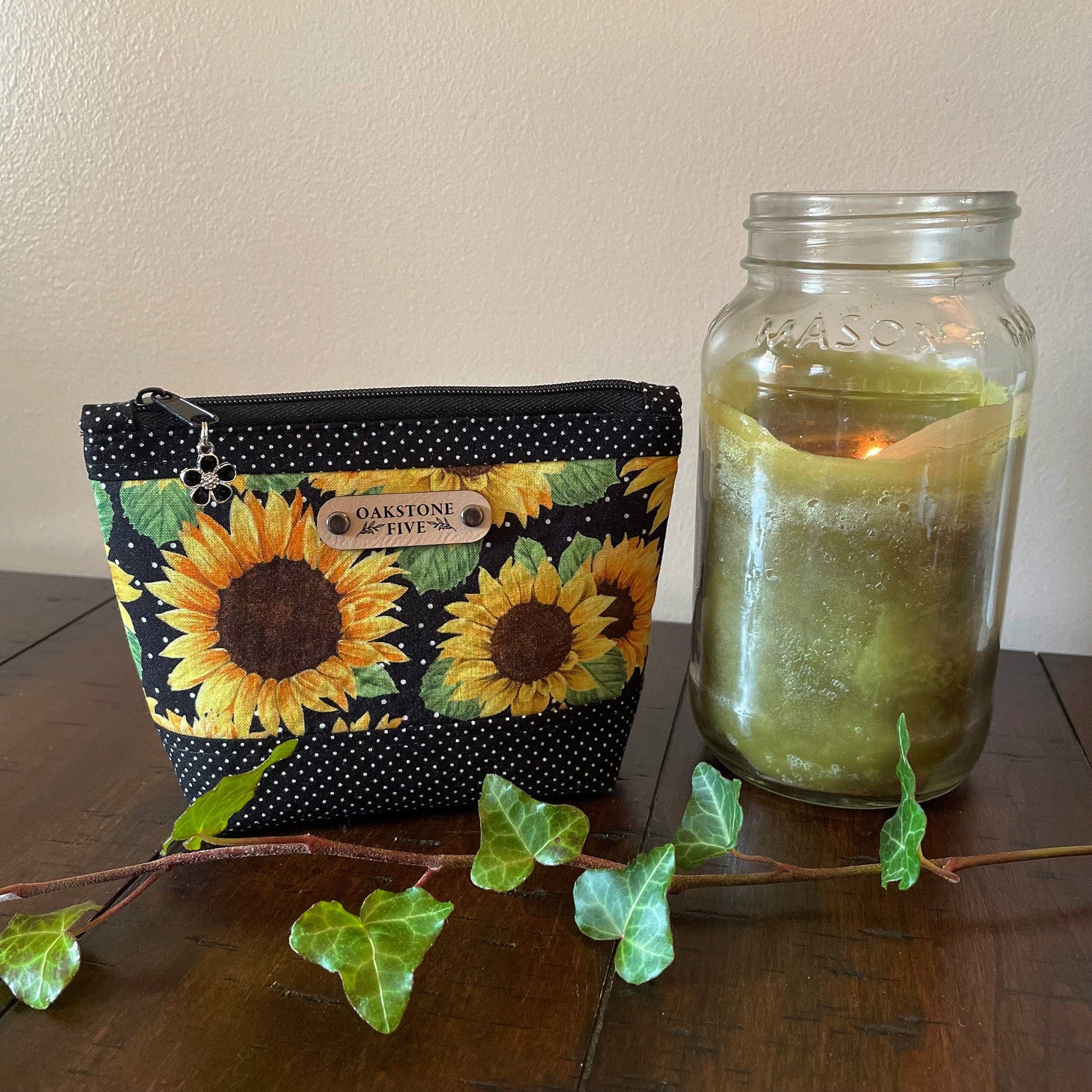A small sized sunflower zipper pouch on a wooden surface with a candle and ivy