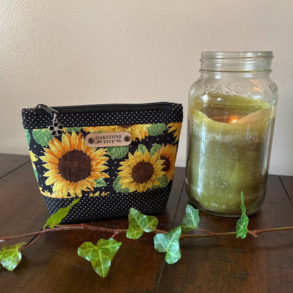 A small sized sunflower zipper pouch on a wooden surface with a candle and ivy