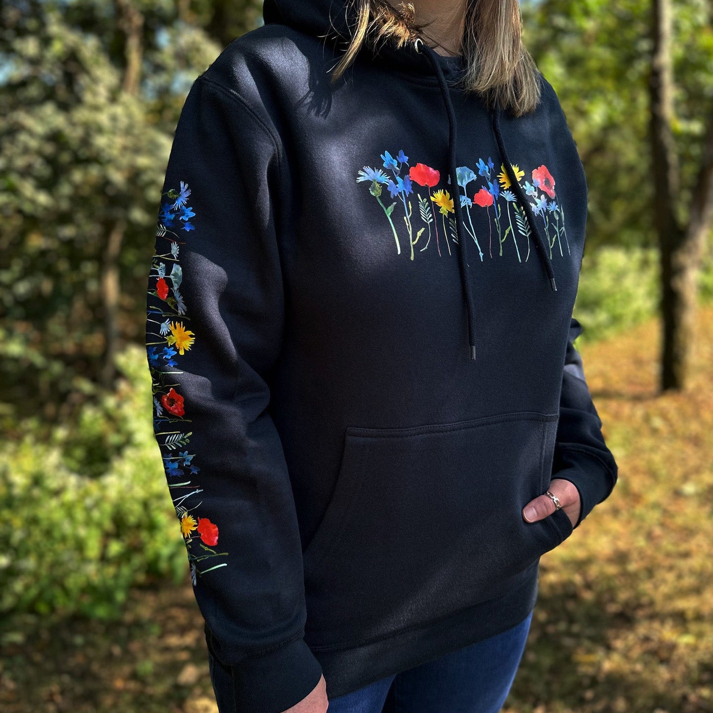 Woman wearing a navy hoodie with floral designs on the sleeves and chest, standing outdoors.