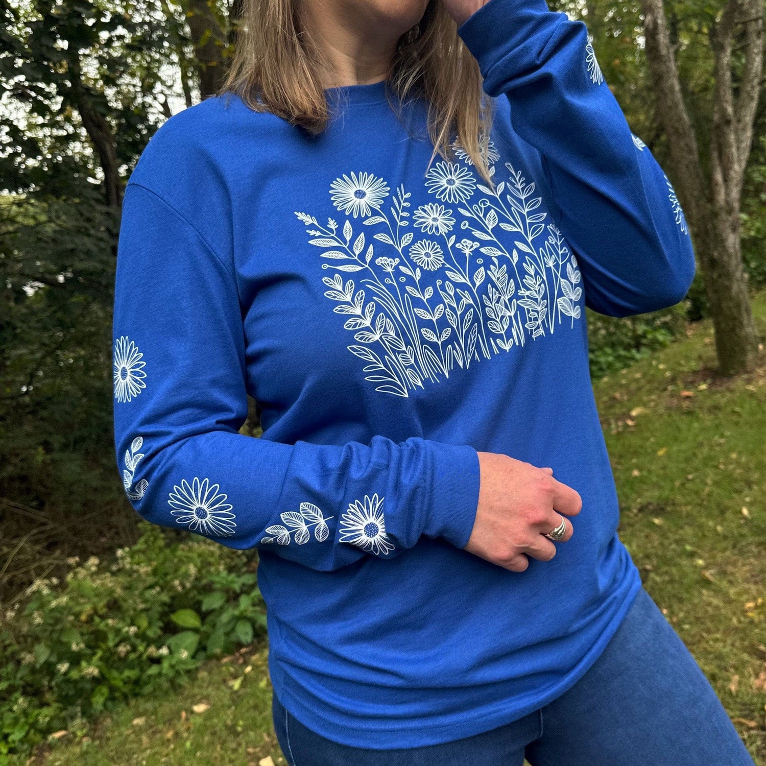 Woman standing outdoors wearing a royal blue long sleeve t-shirt that has white wildflowers on the front and down both sleeves.