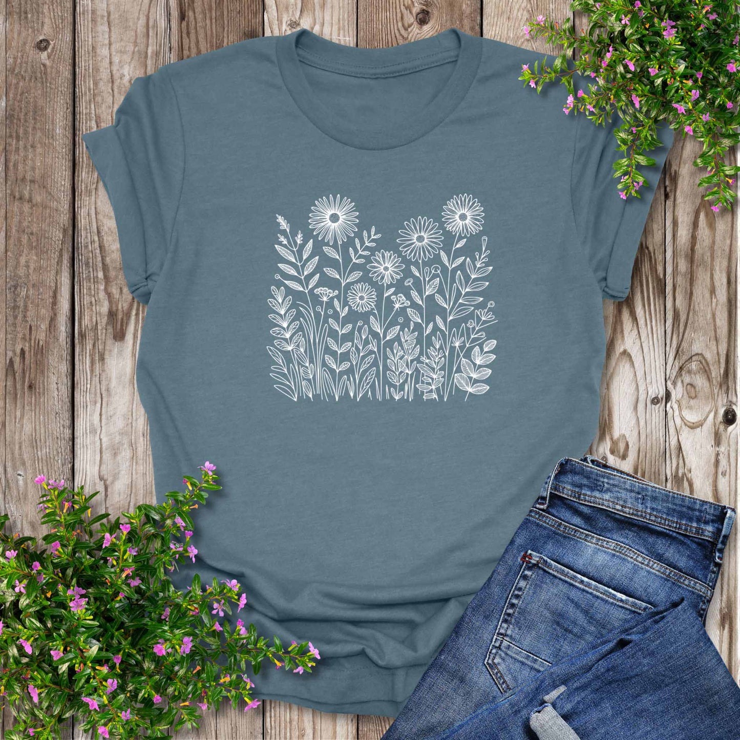 Blue t-shirt with white floral design on a wooden surface with jeans and flowers.