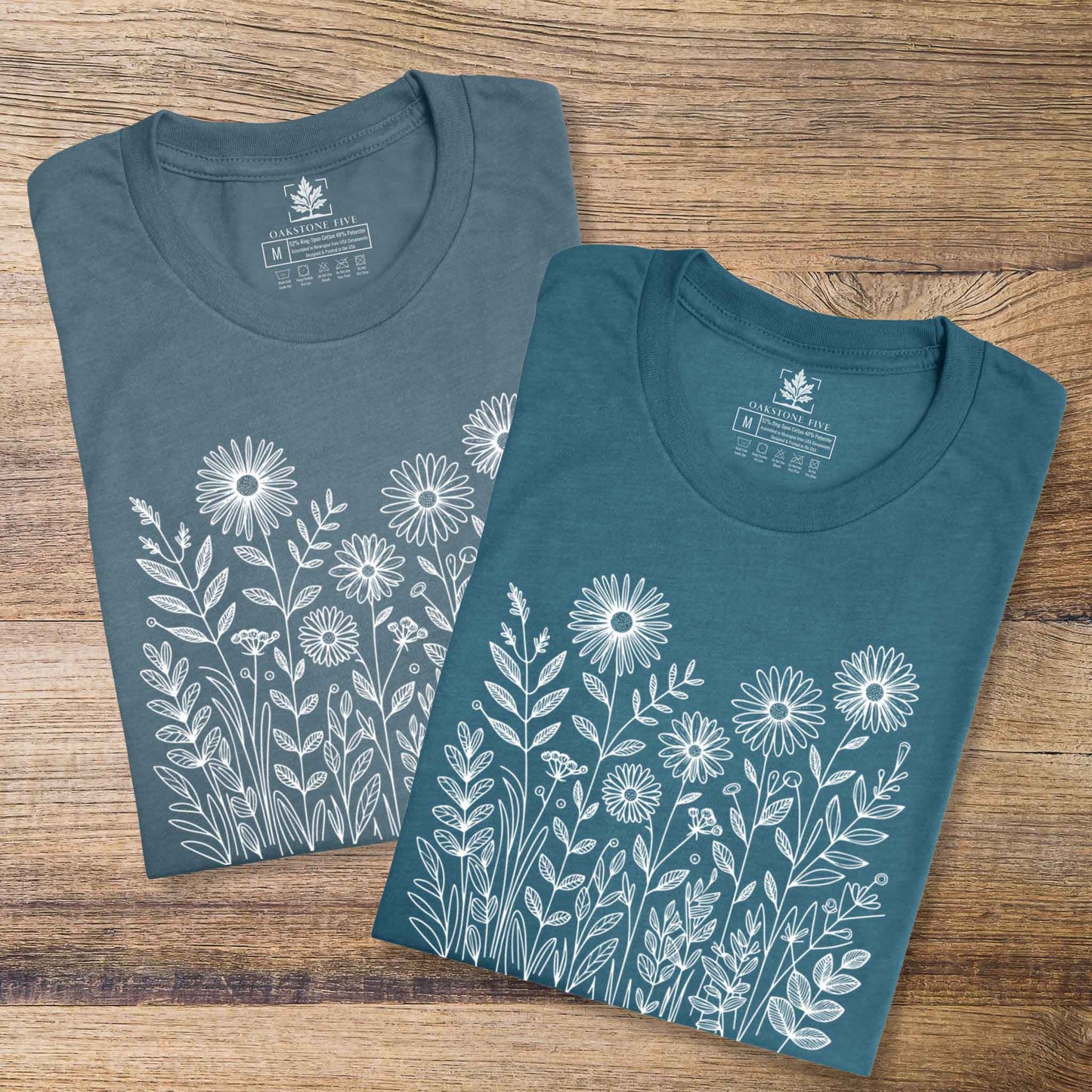 Two blue t-shirts with white floral designs on a wooden surface