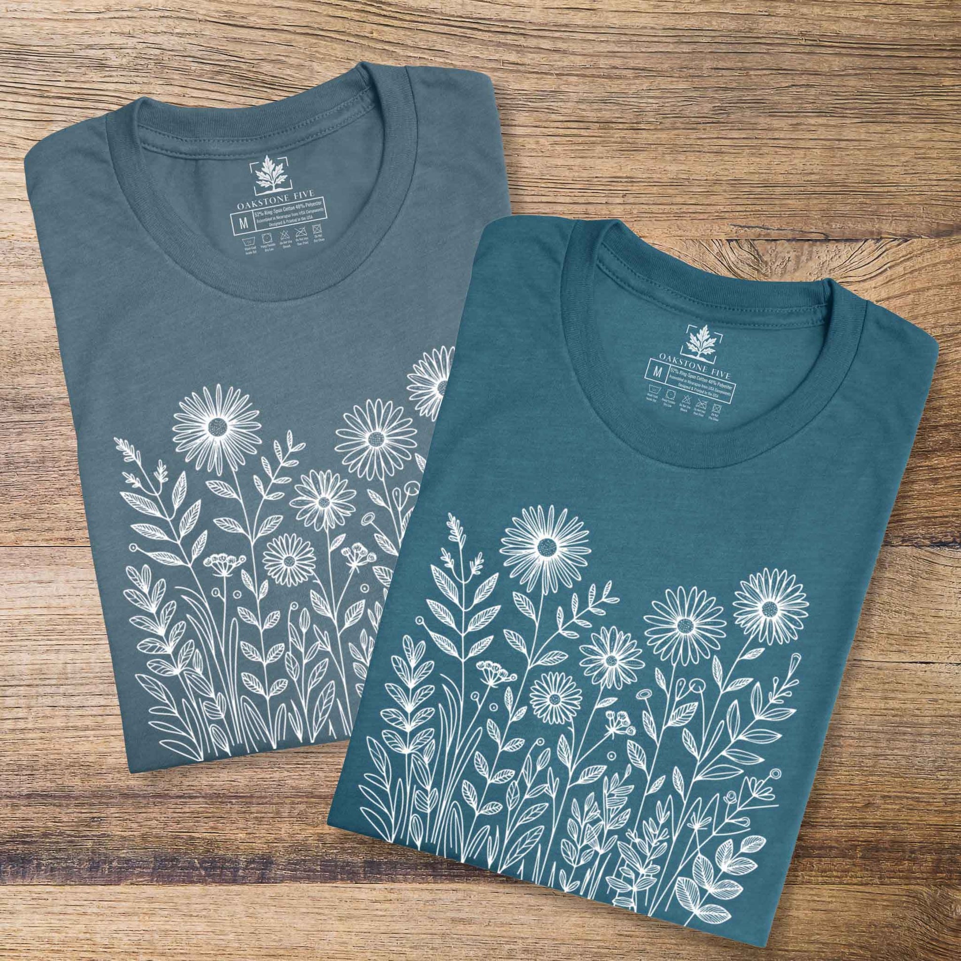 Two blue t-shirts with white floral designs on a wooden surface