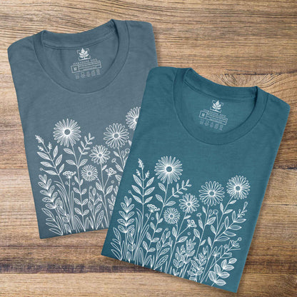Two blue t-shirts with white floral designs on a wooden surface