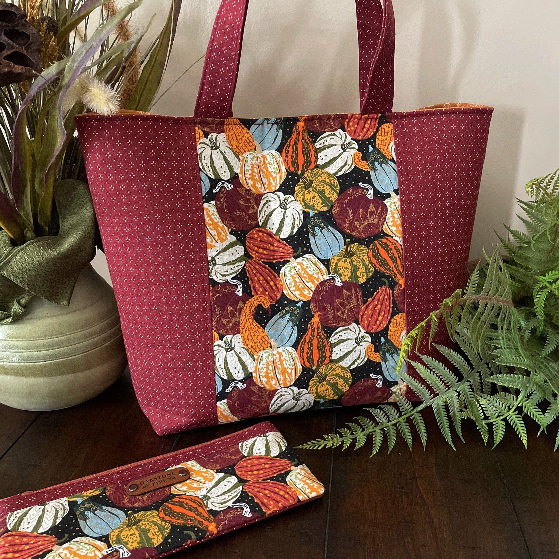 Handmade seasonal tote bag with pumpkin and gourd fall pattern and matching zipper pouch, on a wooden table with plants