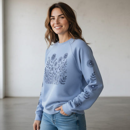 Woman wearing a light purple sweatshirt with floral pattern on front and down the sleeves, against a plain background