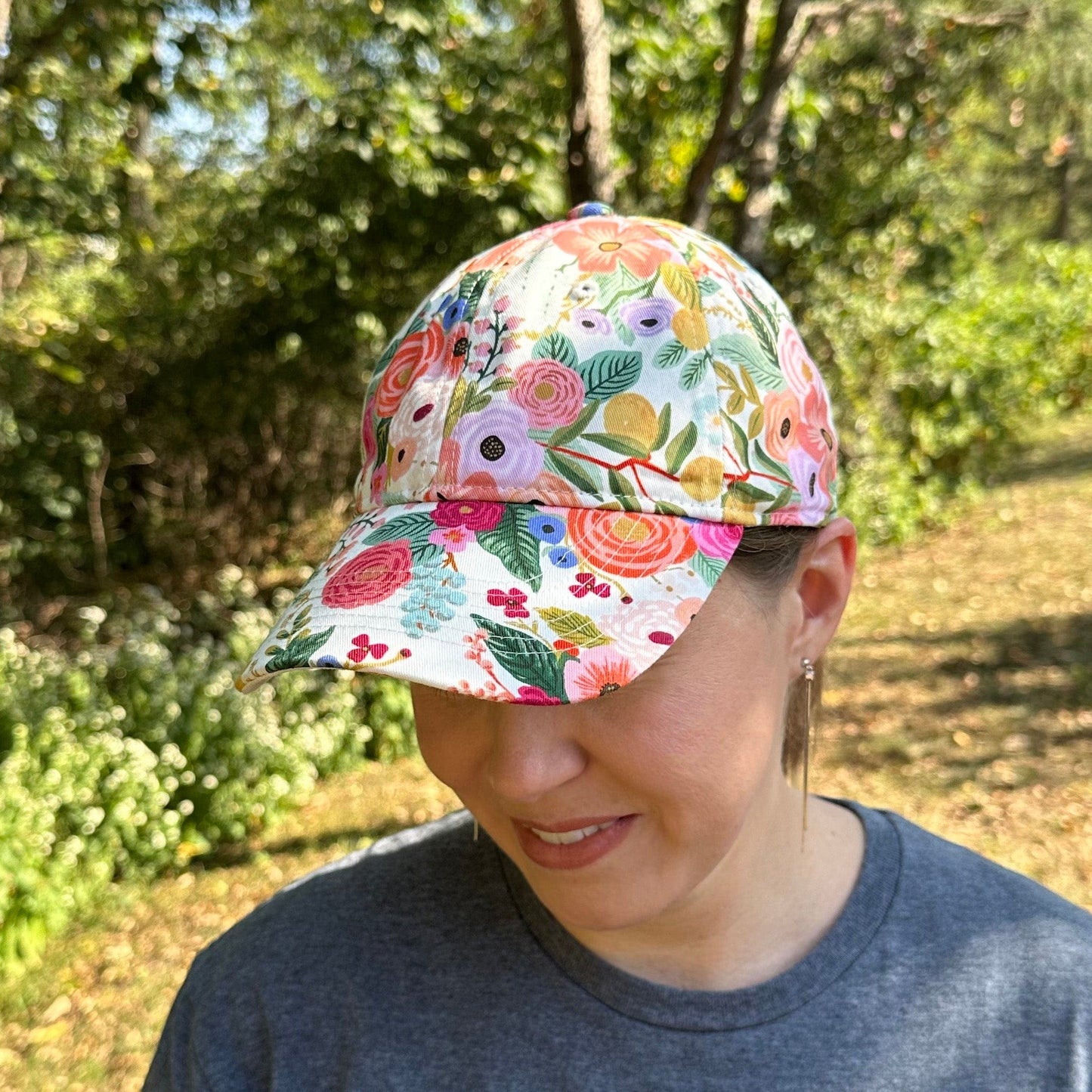 Woman wearing a colorful floral cap outdoors with greenery in the background