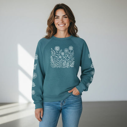 Woman wearing a teal sweatshirt with white floral print on the front and down both sleeves, against a plain background