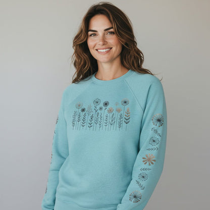 Woman wearing a light blue sweatshirt with floral pattern on the front and both sleeves, on a plain background
